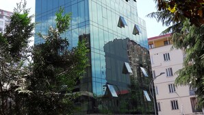 A modern glass building with a reflective facade, surrounded by trees and other buildings. - Hotel Green Glass (Batumi)