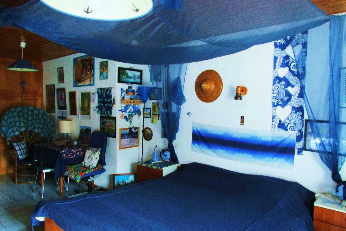 A bedroom with a bed, a desk, and a chair. There are various decorations on the walls, including pictures and a clock.