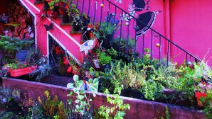 A vibrant staircase with a red wall, adorned with various plants and a whimsical mural. - Tilly's B&B (Le Hohwald)