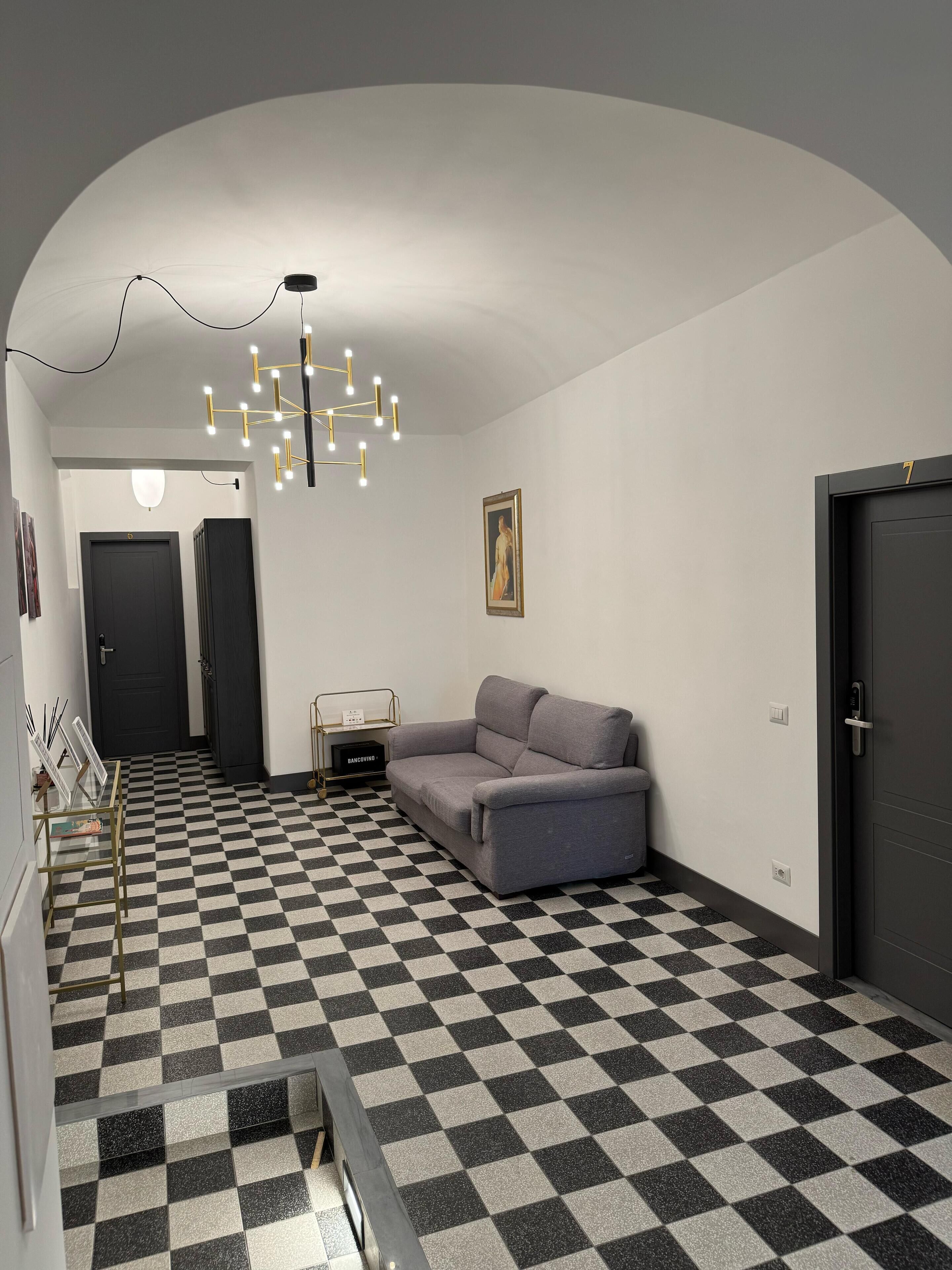 A modern interior with a checkered floor, a grey sofa, a black door, and a unique chandelier.