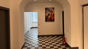 A hallway with a checkered floor, a painting on the wall, and a fire extinguisher. - Santa Monica Townhouse (Rome)