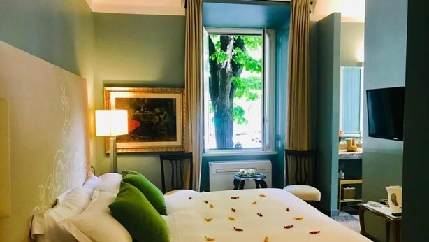 A hotel room with a bed, a window with curtains, a desk with a lamp, and a television. - Santa Monica Townhouse (Rome)