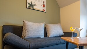 En moderne stue med en mørkegrå sofa, to puder med mønster, en billedramme over sofaen, og et træsofabord med et martini-glas.