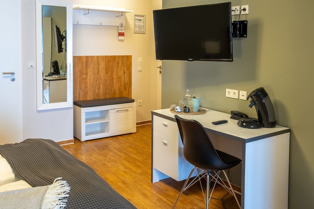 Une chambre d’hôtel de taille réduite, comprenant un lit, un bureau avec une chaise, une télévision et une machine à café.