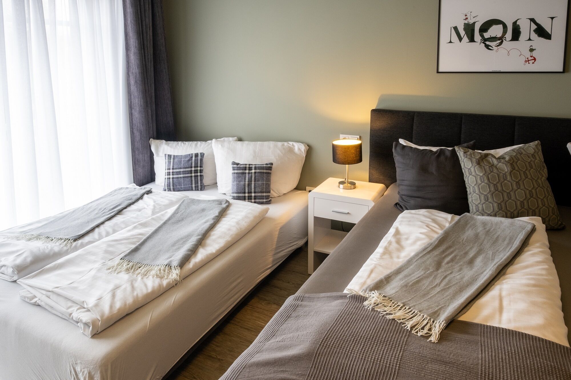 A hotel room with two beds, a nightstand with a lamp, and a wall-mounted artwork.