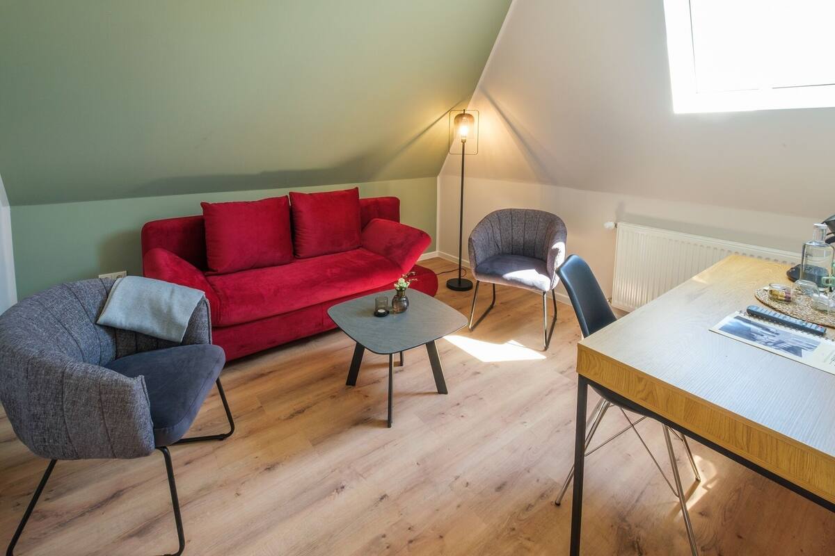Un salon chaleureux avec un canapé rouge, deux fauteuils, une table basse et un lampadaire.