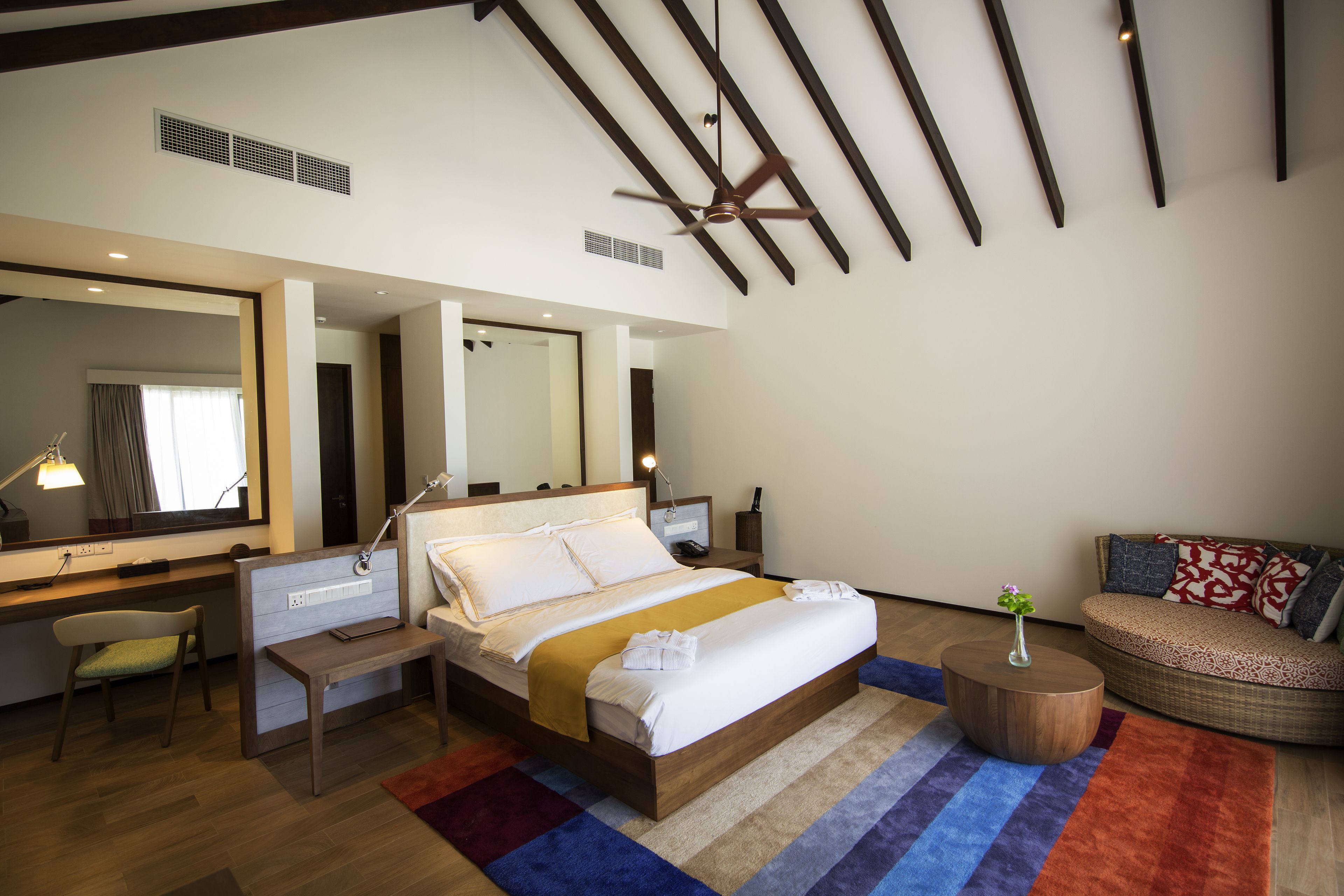 Une chambre d’hôtel moderne équipée d’un grand lit, d’un bureau, d’une chaise, d’un canapé et d’un ventilateur de plafond.
