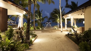 A pathway leading to a beachside resort with palm trees and a view of the ocean.