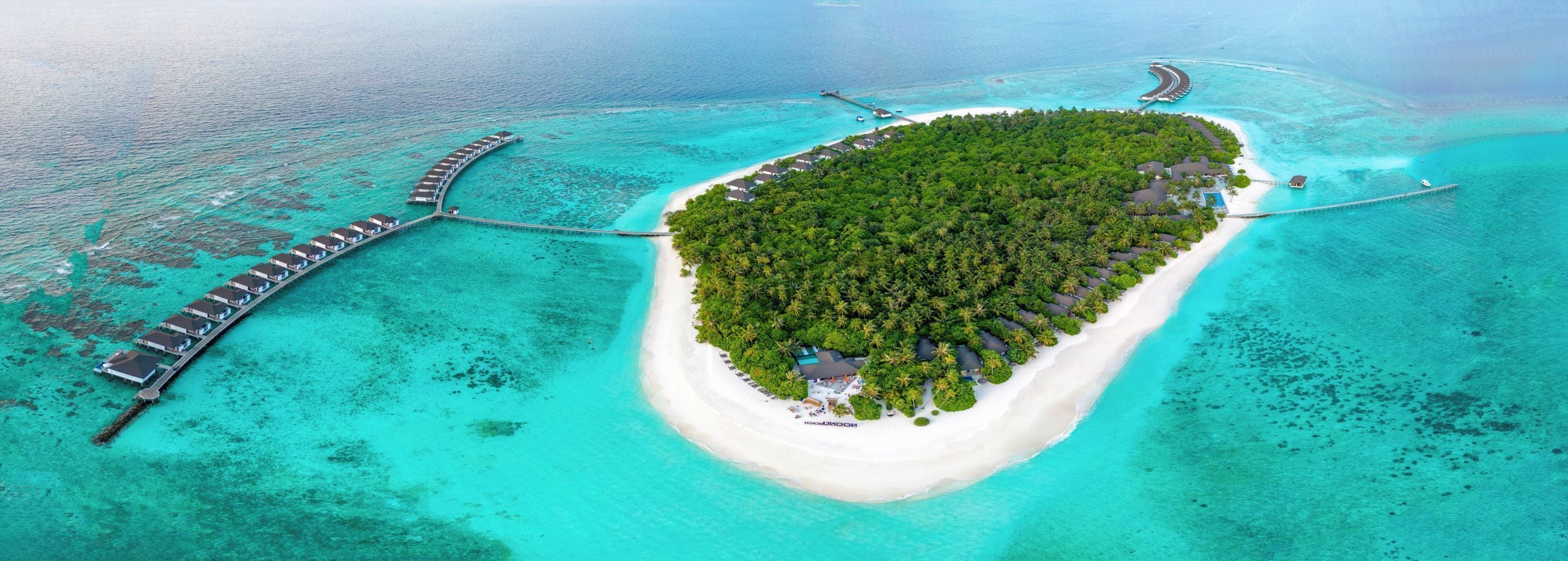 Vue aérienne d’une île tropicale avec une plage de sable blanc, une forêt verdoyante et luxuriante, et une longue jetée s’étendant dans des eaux turquoise.