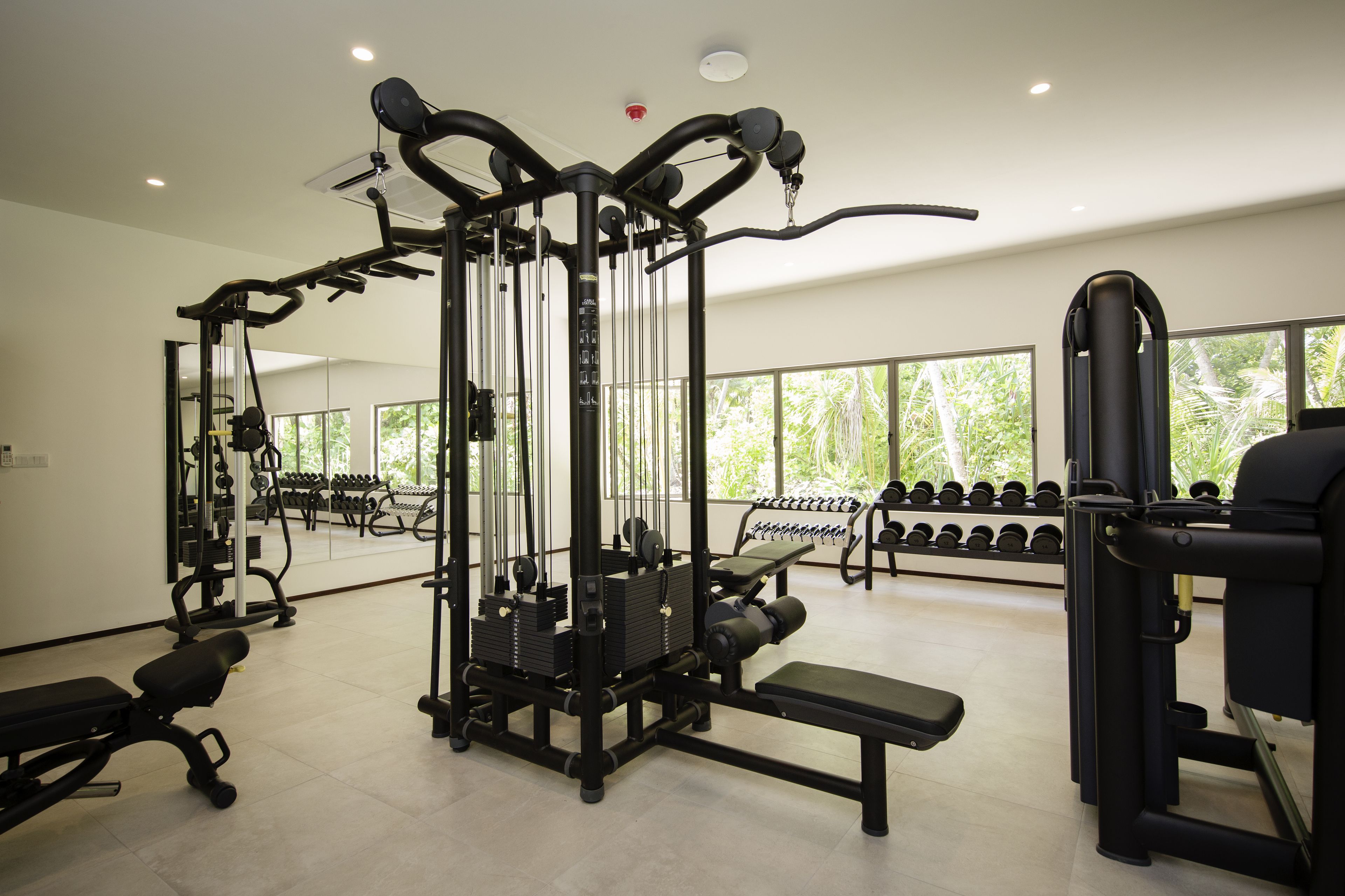 Un gimnasio con varios equipos de ejercicio, bancos y mancuernas.