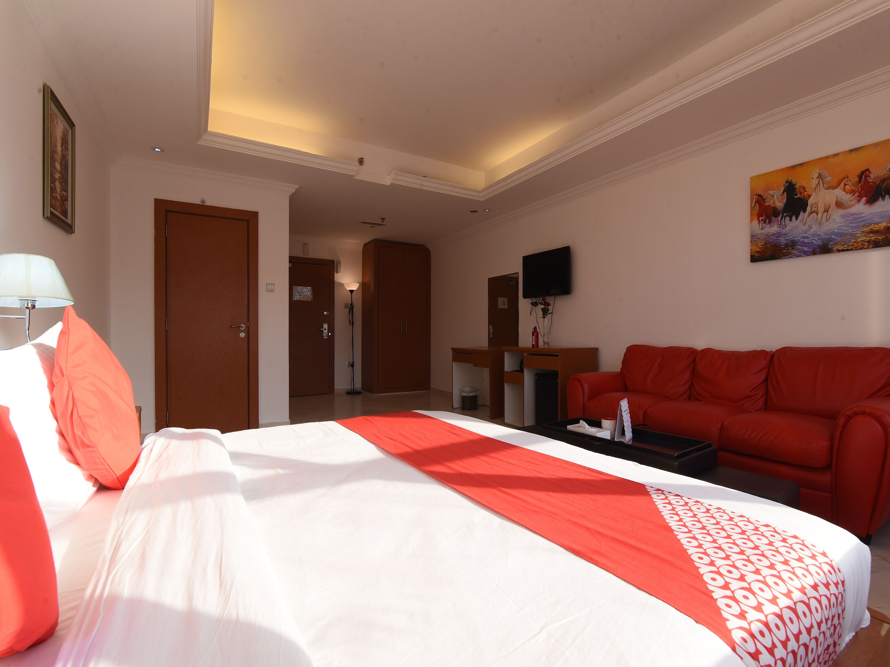 A hotel room with a bed, a red sofa, a desk, and a television.