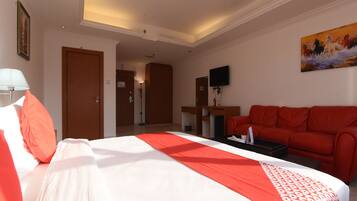 A hotel room with a bed, a red sofa, a desk, and a television.