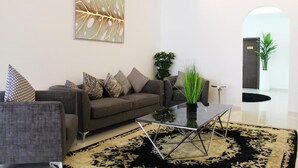 Un salón moderno con un sofá gris, alfombra con estampado negro y dorado, y una mesa de centro de vidrio.
