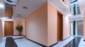 Un pasillo amplio con diseño moderno, que presenta una combinación de pisos de baldosas blancas y negras, una gran planta en maceta y una puerta de madera.