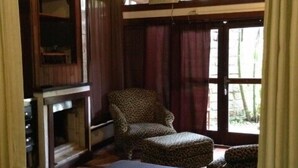 A room with a bed, a leopard-print ottoman, a chair, a fireplace, and a window with curtains. - Pousada Aloha Beach House (Imbituba)