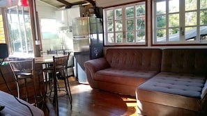 A cozy living area with a sofa, a dining table with chairs, and a kitchen in the background. - Pousada Aloha Beach House (Imbituba)