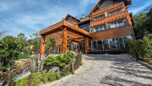 A modern multi-story house with a wooden exterior, large windows, and a stone pathway leading to the entrance. - Hotel Refúgio da Montanha - 900m da Rua Coberta (Gramado)