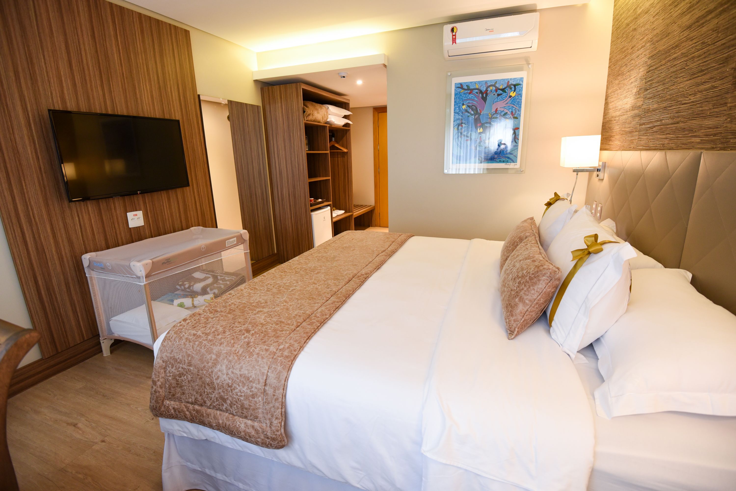 Una habitación de hotel con una cama grande, un televisor montado en la pared, un armario y un escritorio pequeño.