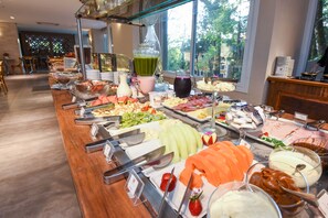 A buffet with various food items and beverages, including fruits, cheeses, and a green smoothie.