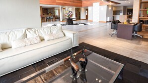A spacious lobby with a modern design, featuring a leather sofa, a glass coffee table with decorative items, and a seating area with chairs and a desk. - Hotel Refúgio da Montanha - 900m da Rua Coberta (Gramado)