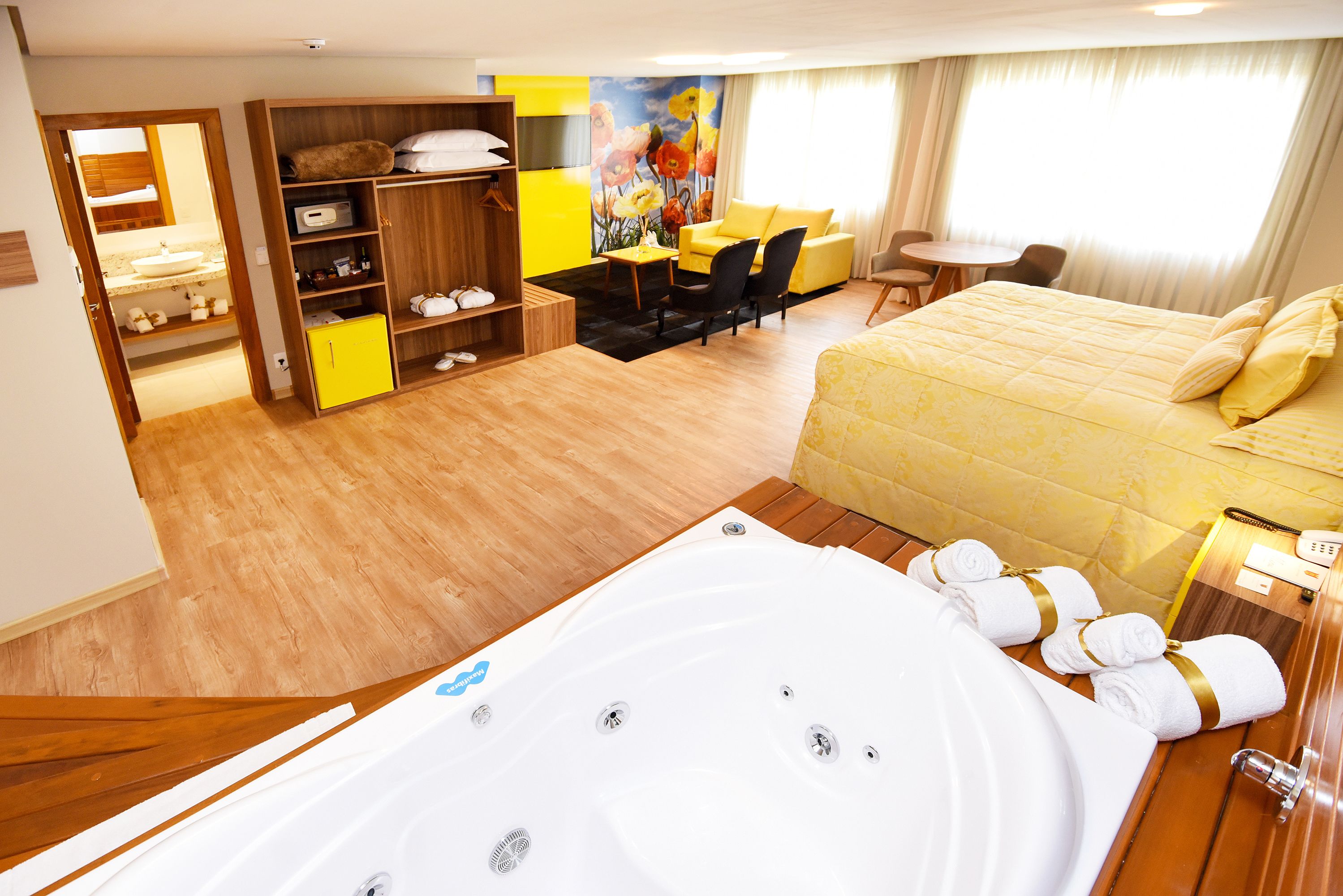 A hotel room with a large bed, a sitting area with a sofa and chairs, a desk, a large window, and a bathroom with a bathtub and towels.