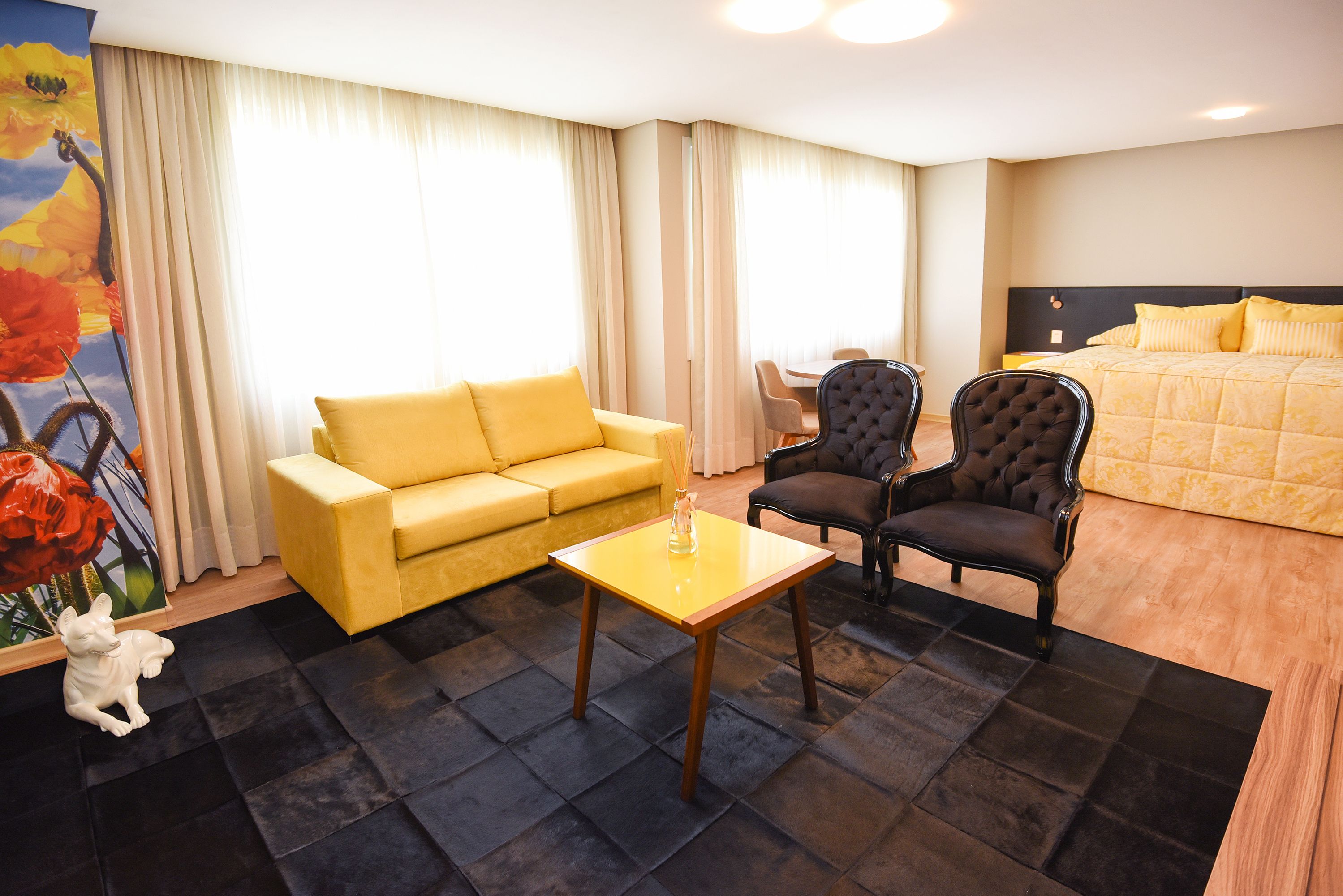 A hotel room with a yellow sofa, two armchairs, a small table, and a bed with yellow bedding.