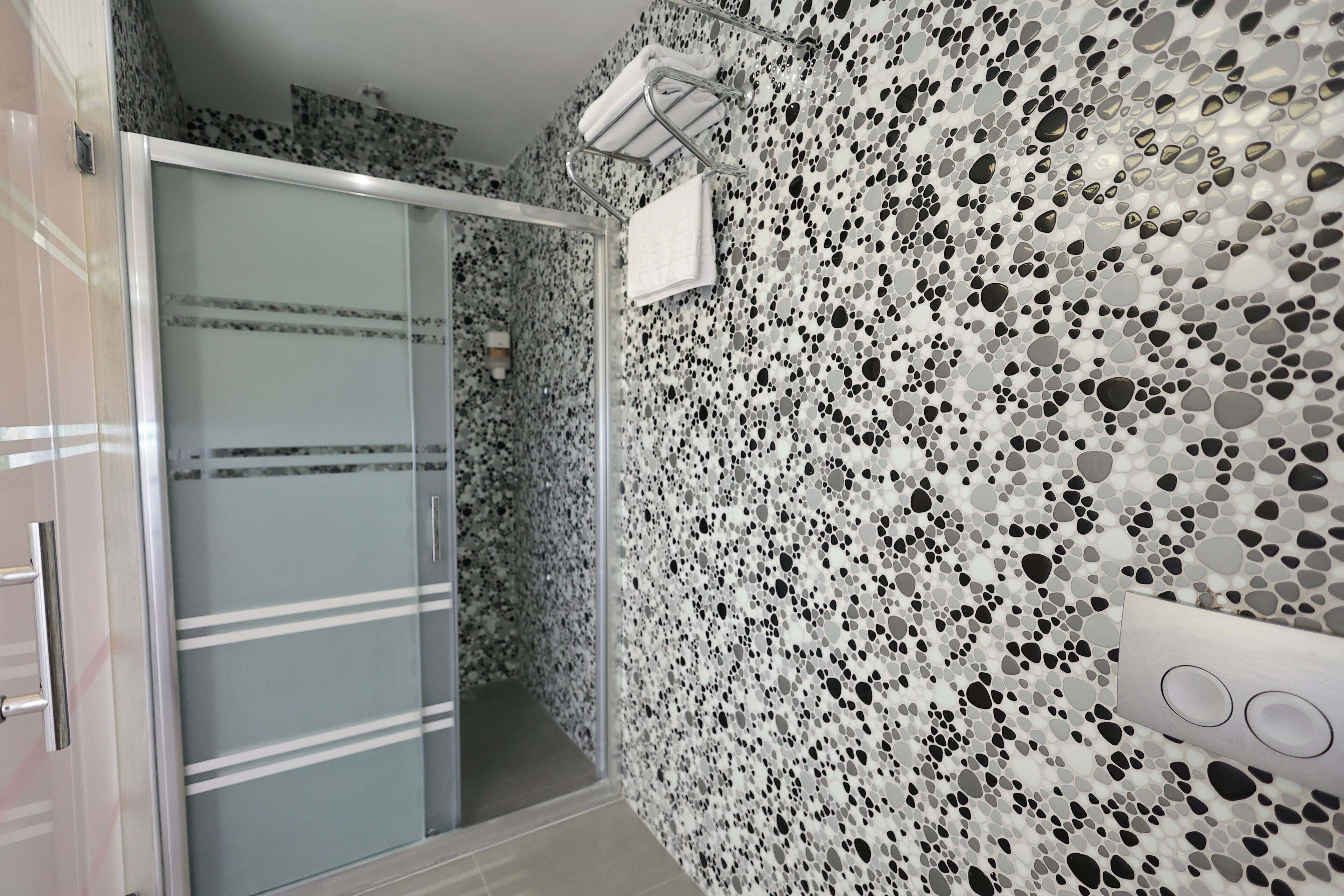 Un baño con pared de baldosas veteadas, cabina de ducha de vidrio y un perchero para toallas.
