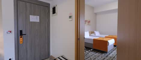 A hotel room with a wooden door, a bed with an orange bedspread, a small table, and a wall-mounted heater.