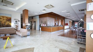 Uma área de recepção de hotel, com balcão de atendimento, espaço para sentar e um quadro grande na parede.