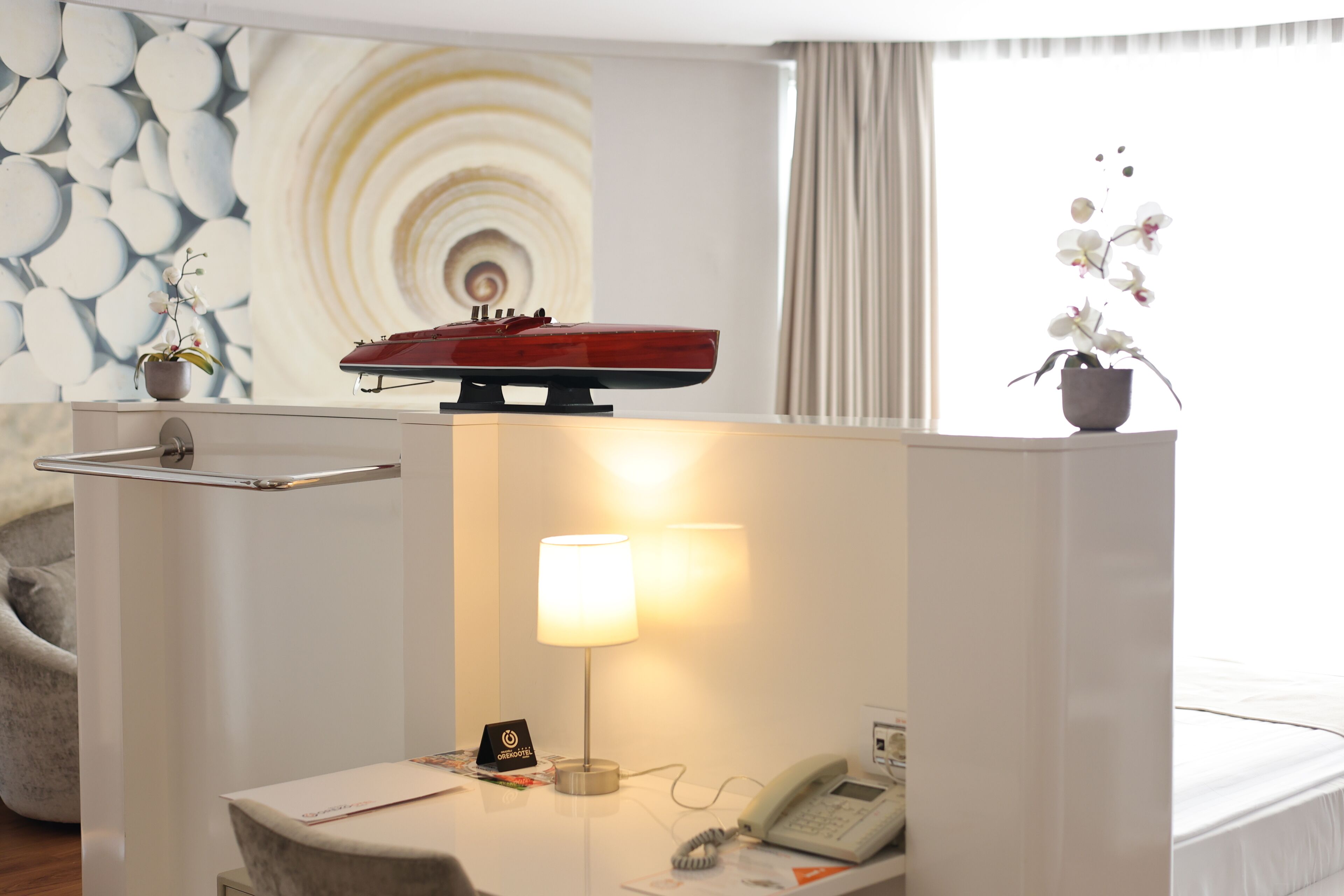Habitación de hotel con escritorio, lámpara, teléfono, una pequeña planta en maceta y un objeto decorativo en el escritorio.