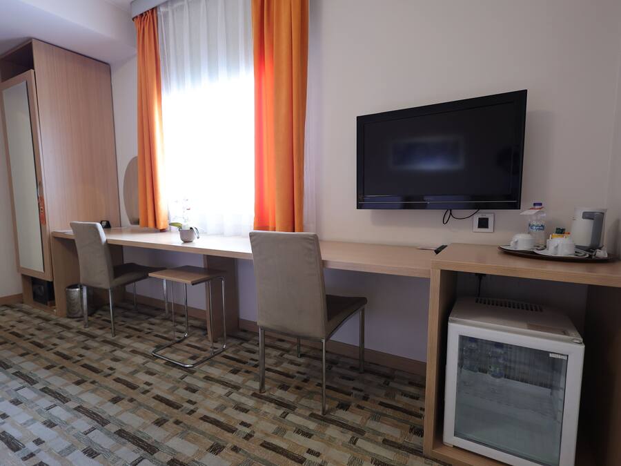 Habitación de hotel con escritorio, dos sillas, televisor, mini refrigerador y armario.