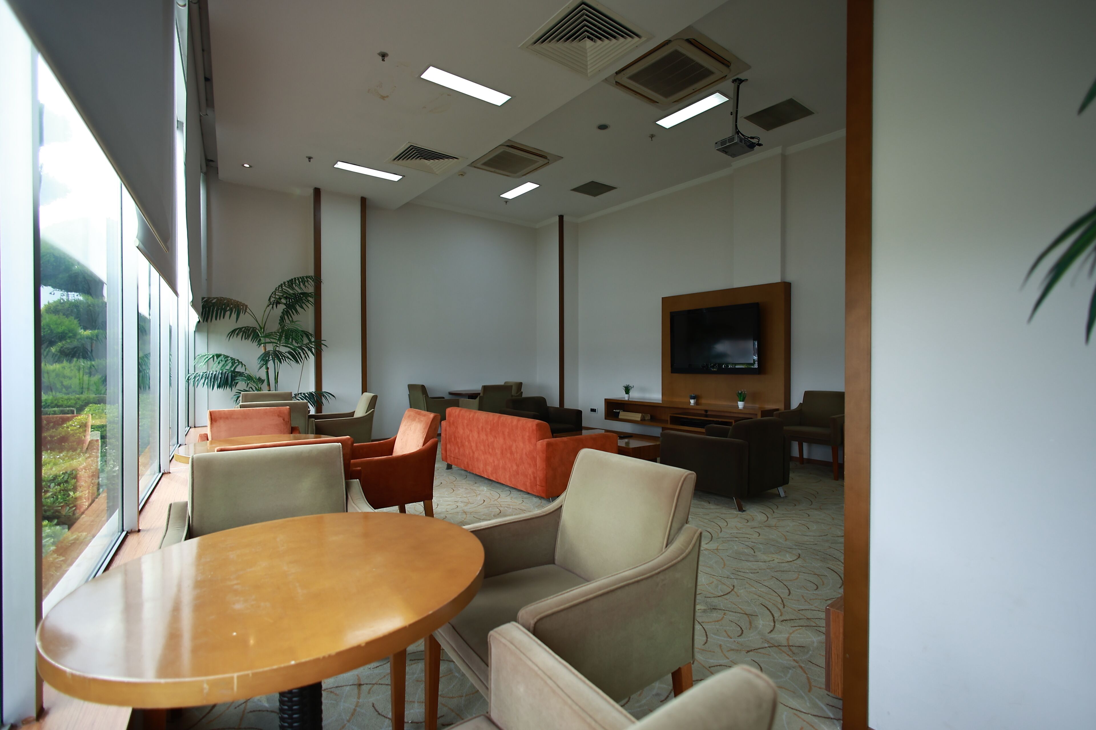 A modern indoor space with a large window, a wooden table, several chairs, a sofa, and a television.