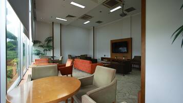 A modern indoor space with a large window, a wooden table, several chairs, a sofa, and a television.