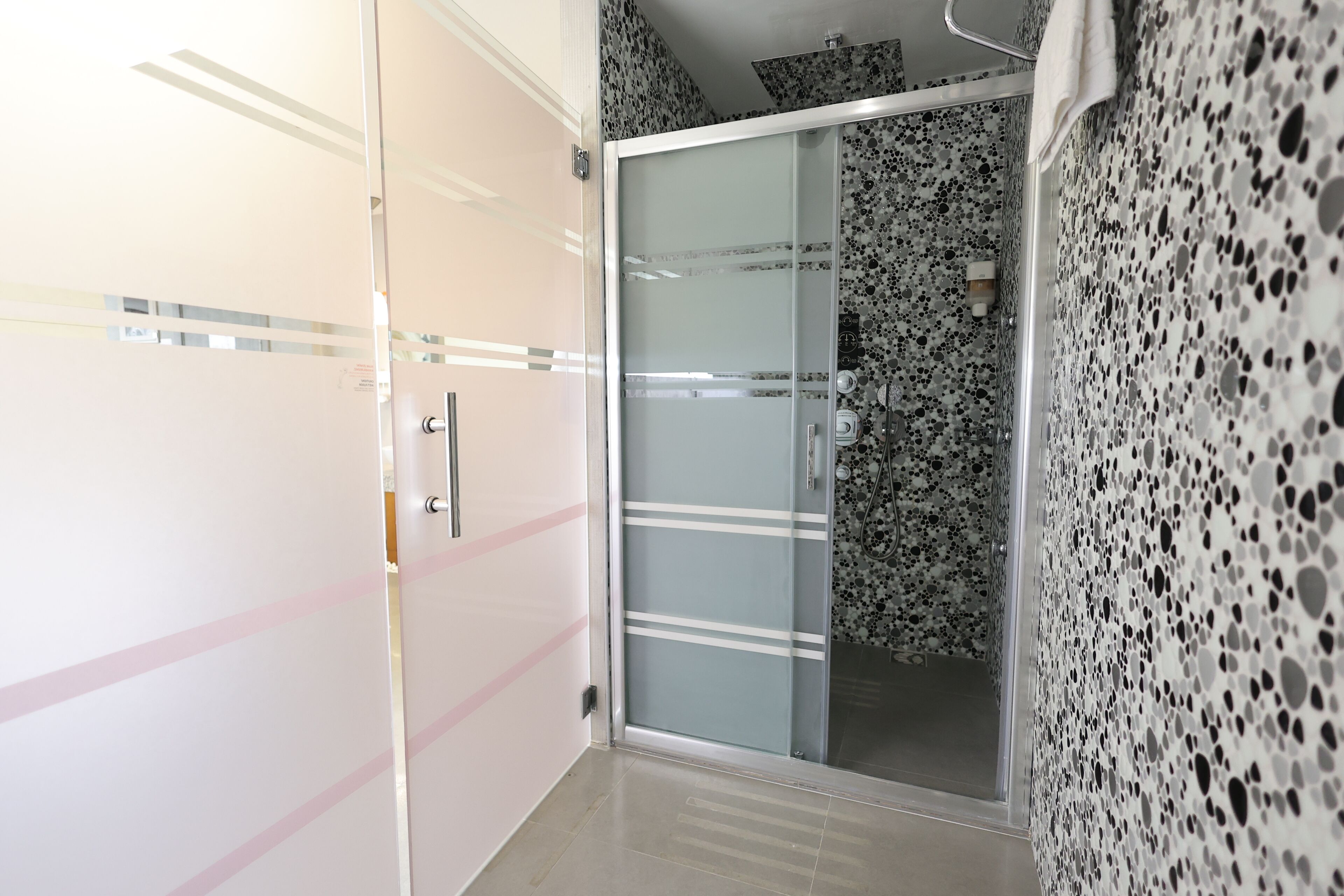 A modern bathroom with a glass shower enclosure, a tiled wall, and a door with a pink stripe.