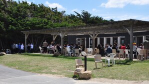 Een terras met tafels en stoelen onder een houten pergola, omgeven door bomen.