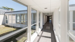 Een gang met glazen wanden, witte zuilen en een betegelde vloer.