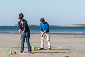 Two people playing croquet on a beach with a clear sky and calm sea in the background.