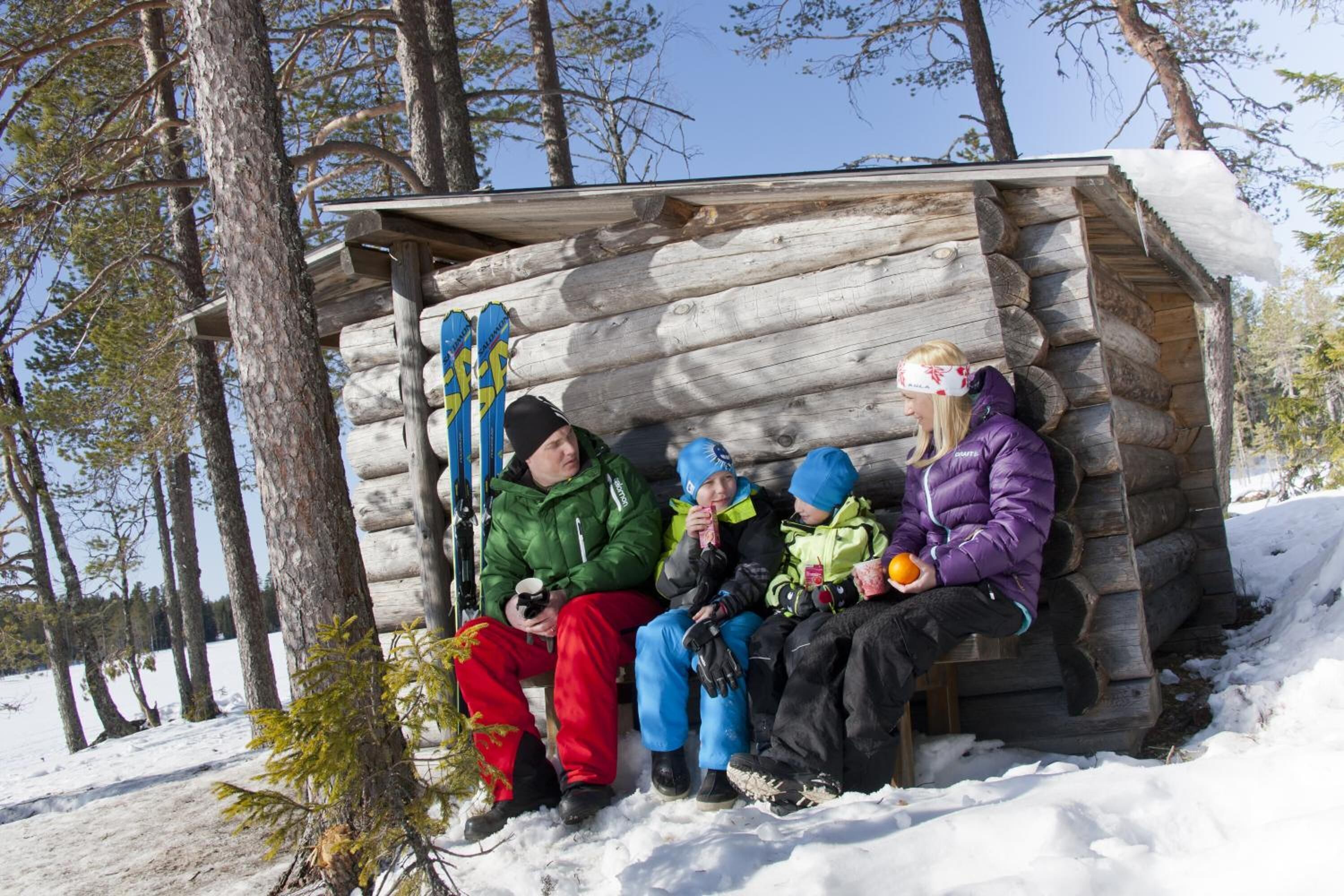A log cabin with a bench outside, surrounded by trees and snow.