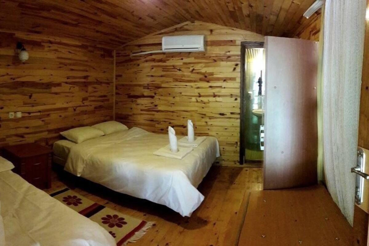 A wooden cabin room with two beds, a small table, and an air conditioning unit.