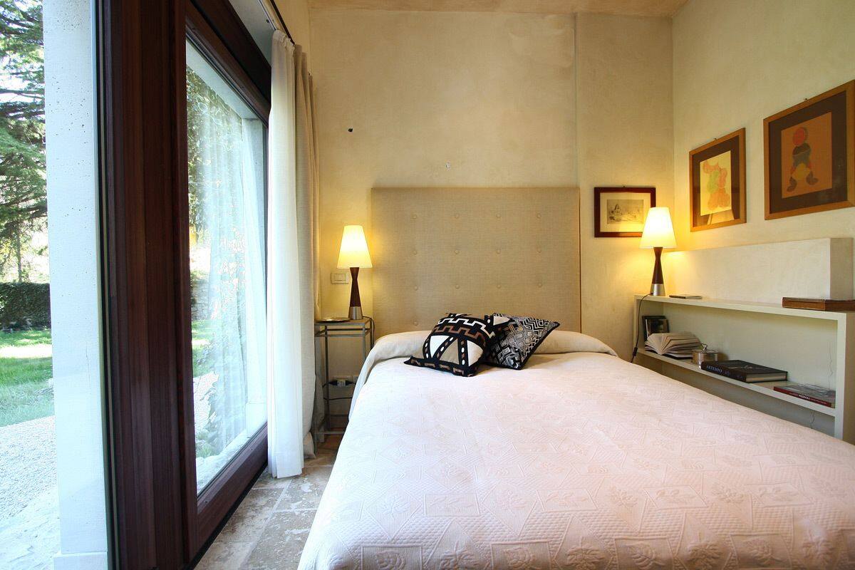 A hotel room with a large bed, two bedside lamps, a nightstand with a lamp, a bookshelf with books, and framed pictures on the wall.