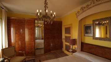A hotel room with a large bed, a chandelier, a wardrobe, a chair, and a mirror on the wall.