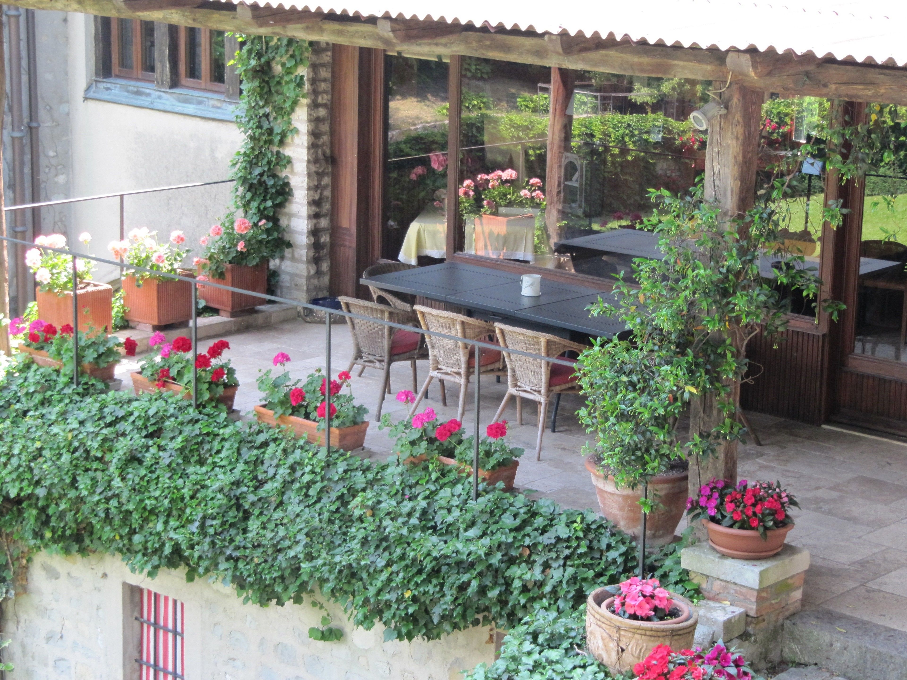 An outdoor patio with a table and chairs, surrounded by potted plants and a stone wall.