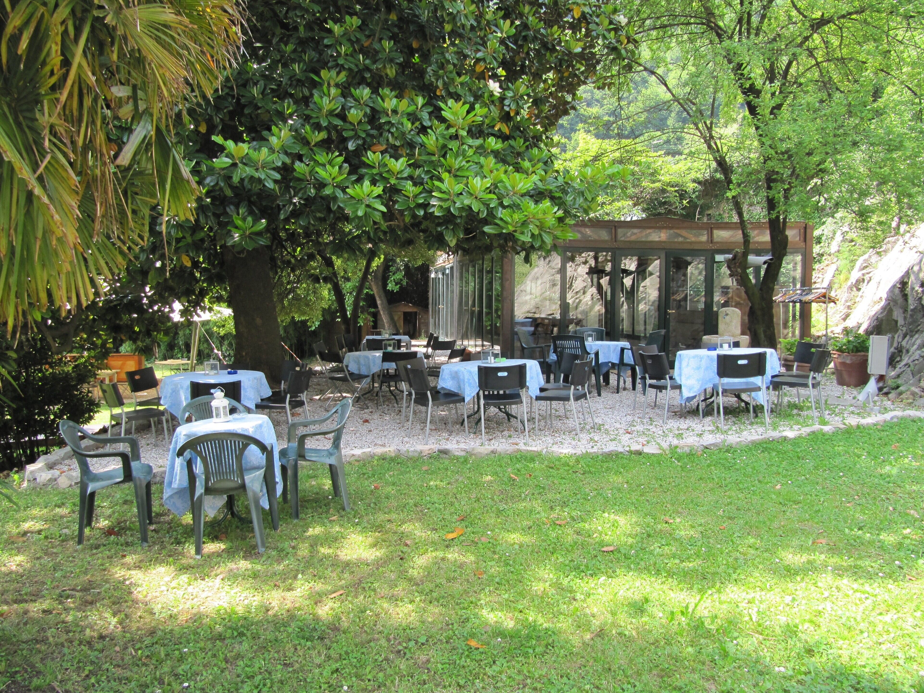 An outdoor patio with tables and chairs, surrounded by trees and a stone structure.