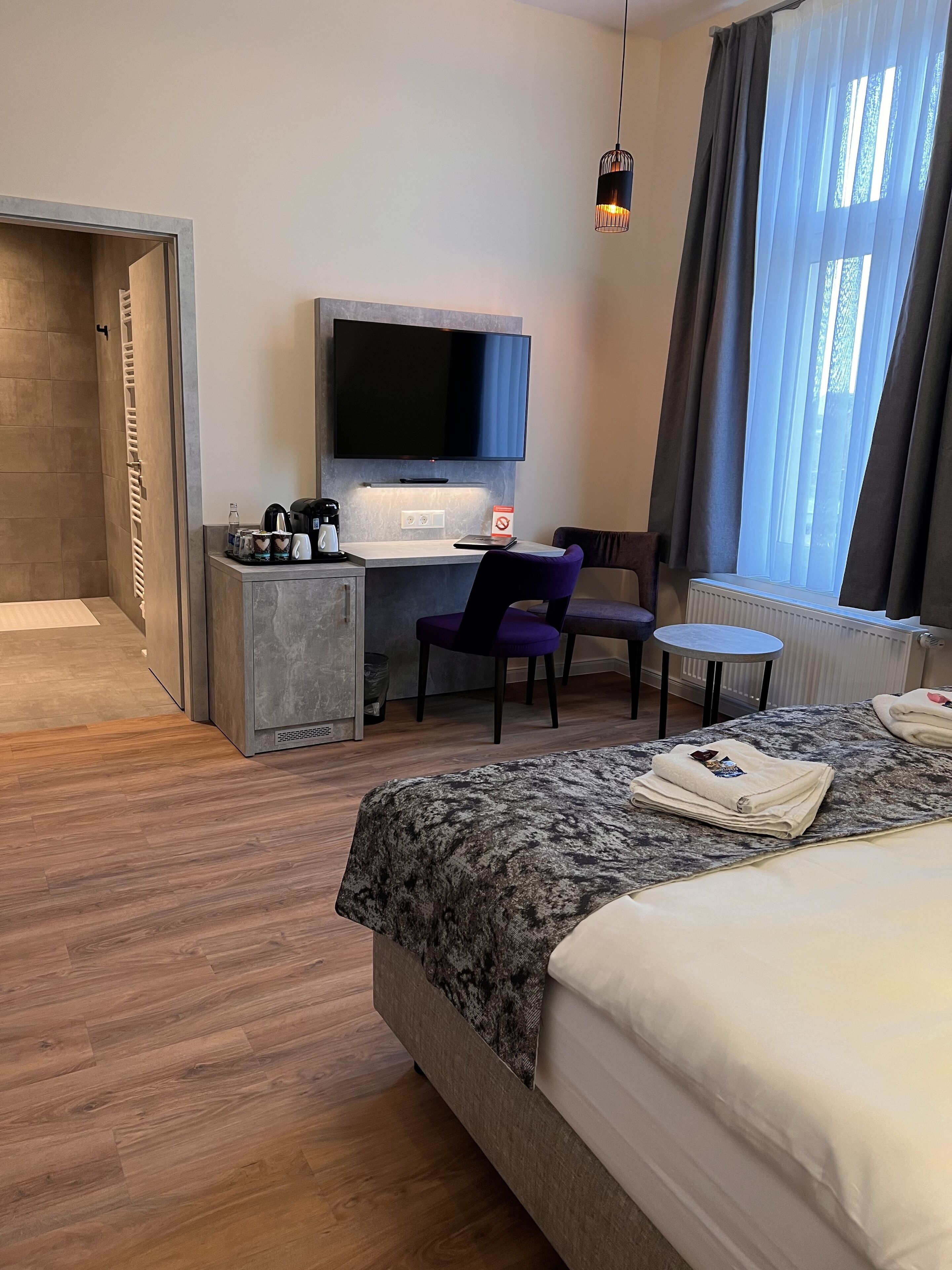 A hotel room with a bed, a desk with a chair, a television, and a small table.