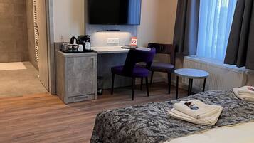 A hotel room with a bed, a desk with a chair, a television, and a small table.