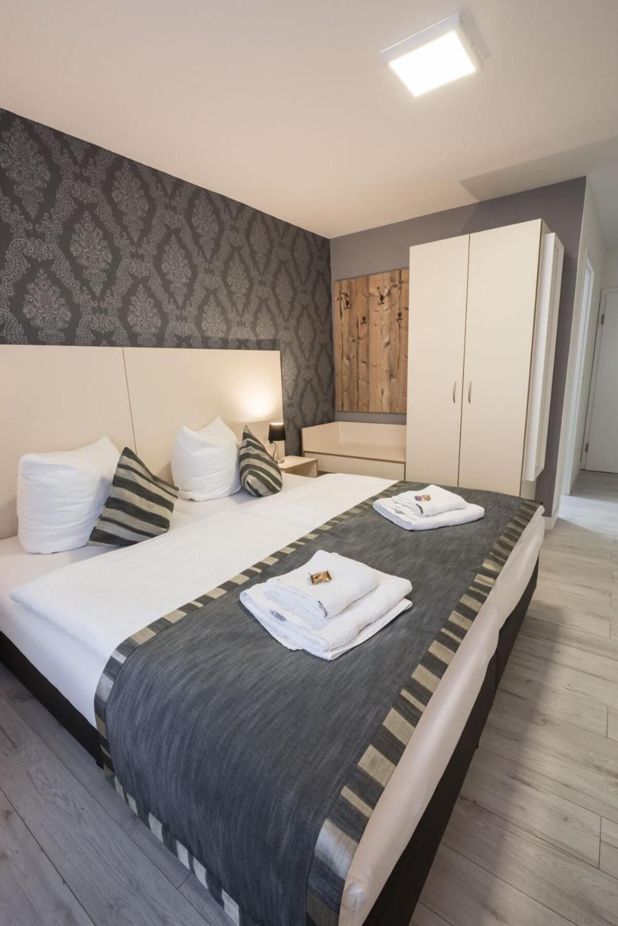 A modern bedroom with a large bed, a wooden wardrobe, and a patterned wall.