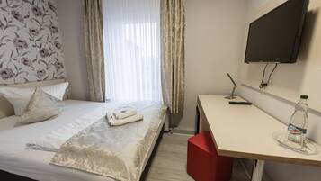 Una habitación de hotel con cama, escritorio, televisión y ventana con cortinas.