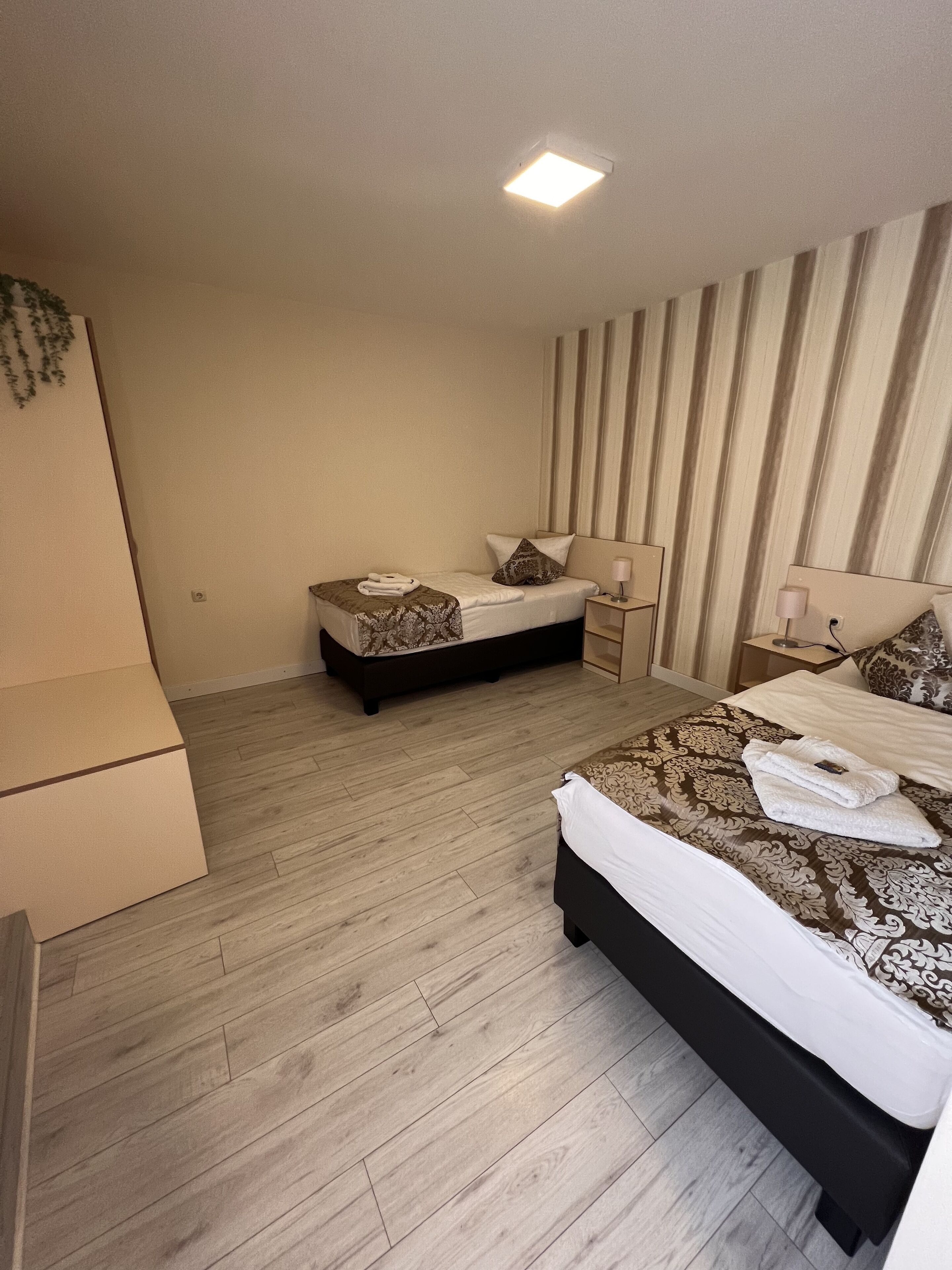 Habitación de hotel con dos camas, piso de madera, una lámpara en el techo y pared a rayas.