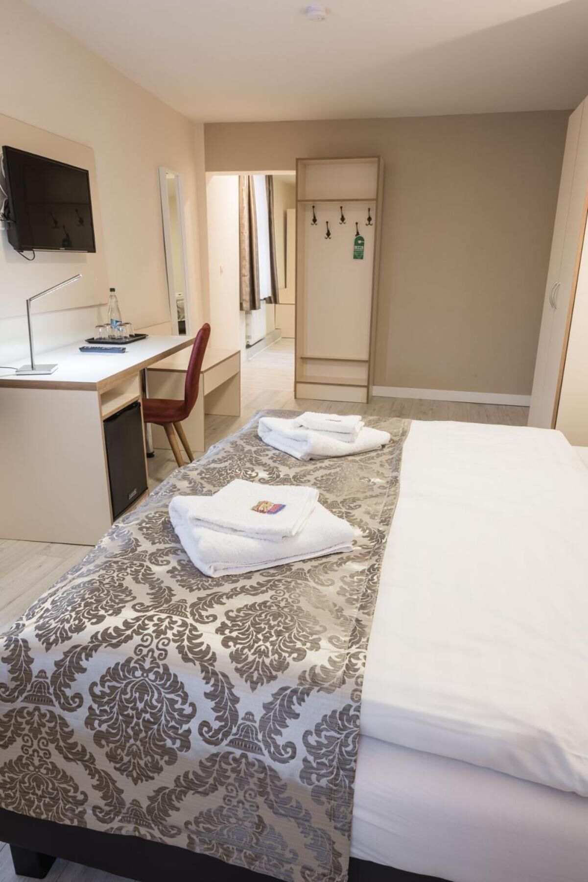 A hotel room with a bed, a desk, a chair, a TV, and a wardrobe.