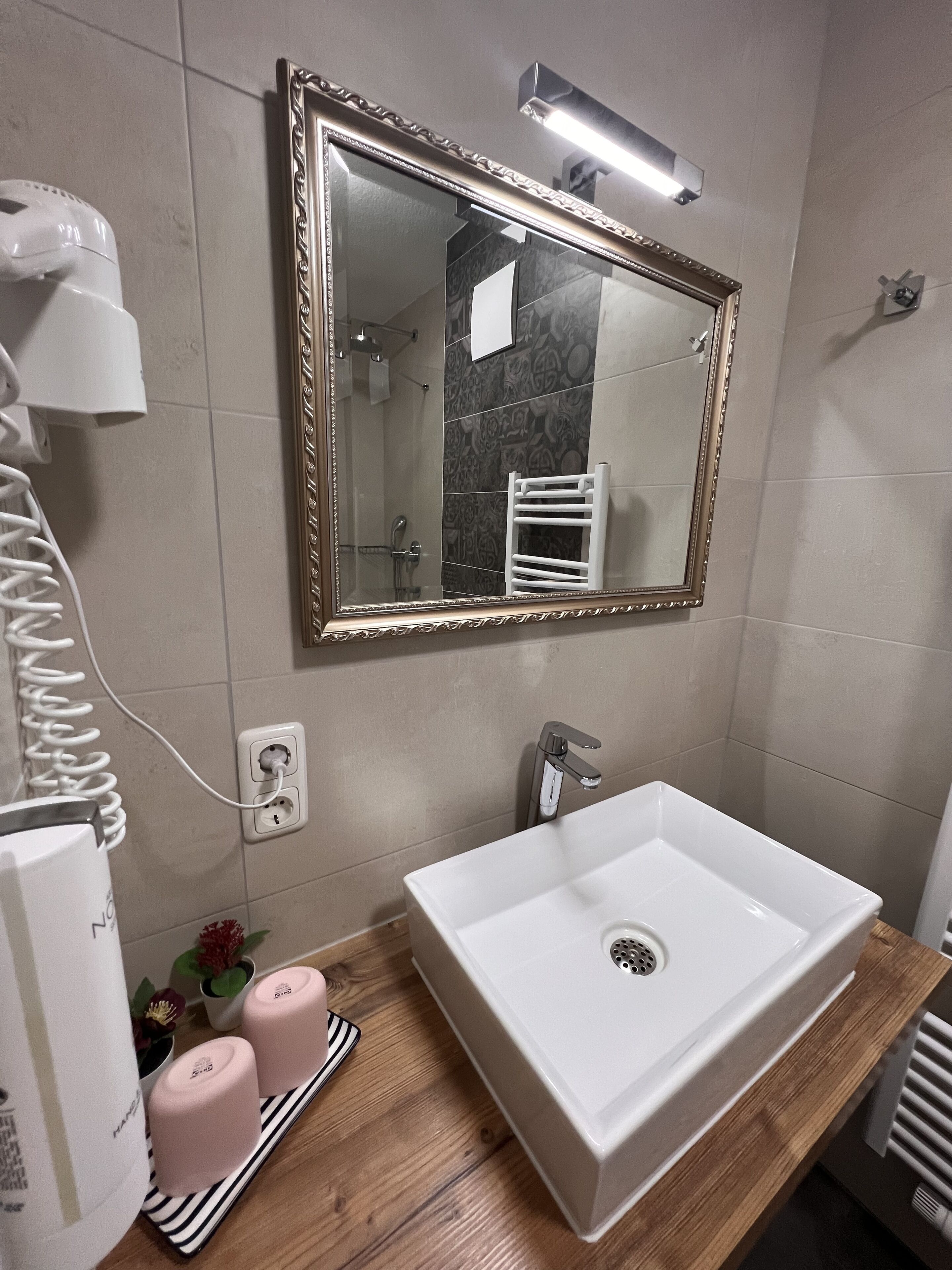 Un baño con un lavamanos blanco, un espejo con marco decorativo, un perchero y un secador de pelo en la encimera.